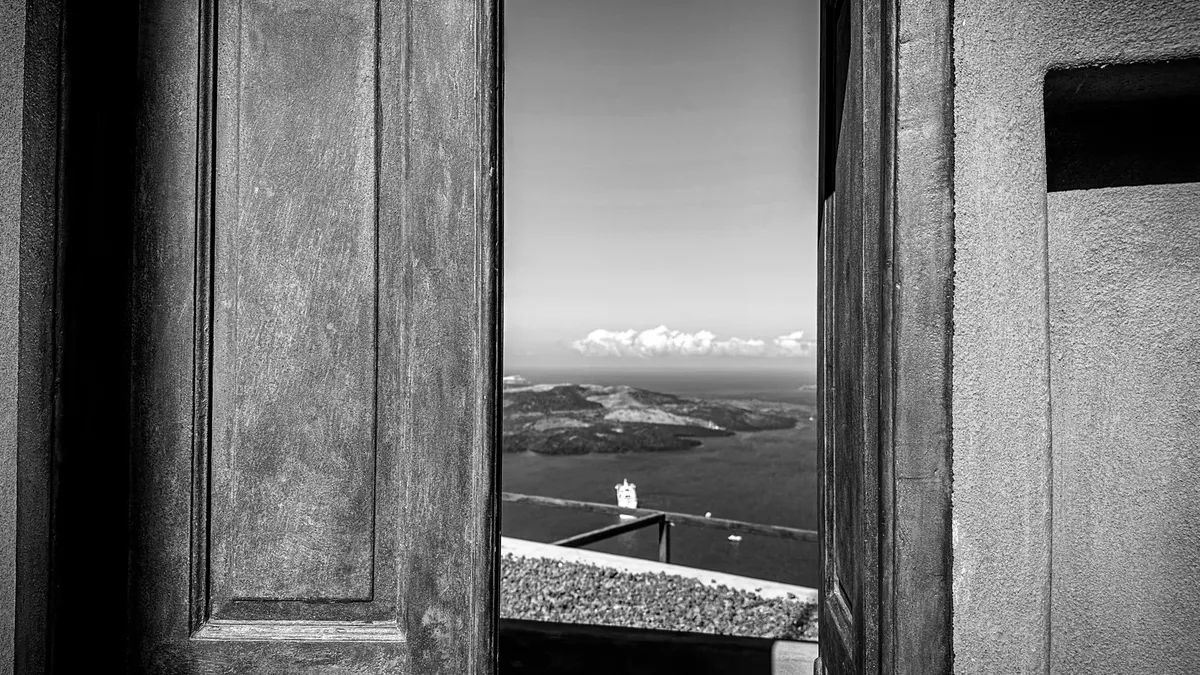 Captivating Santorini seascape viewed through an open door in black and white.