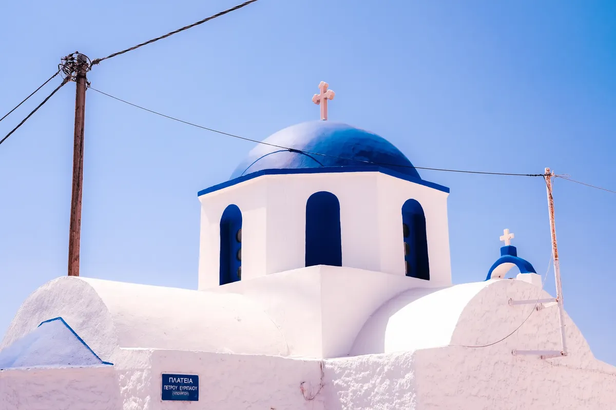 A picturesque blue dome church in Santorini against a bright blue sky, showcasing classic Cycladic architecture.