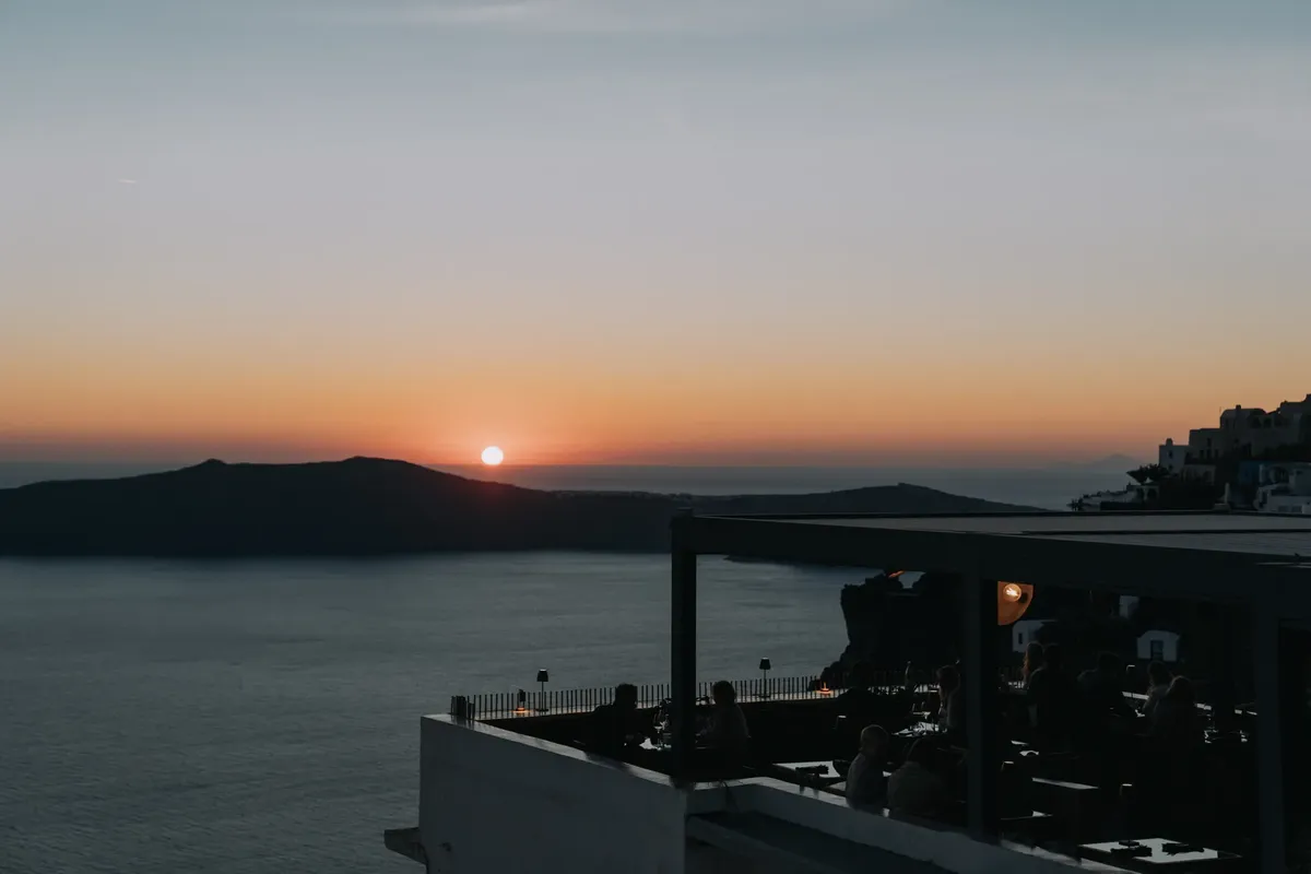 Capturing a serene sunset at a Santorini cafe with silhouettes against the sea.