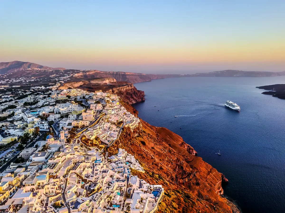 Stunning aerial shot of Santorini coast at sunset with a cruise ship in the Aegean Sea.