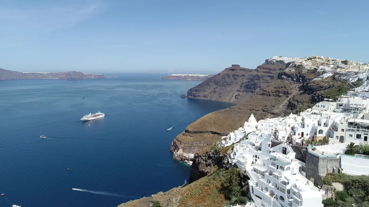 A stunning coastal view of Santorini with white buildings and a cruise ship in the blue sea.