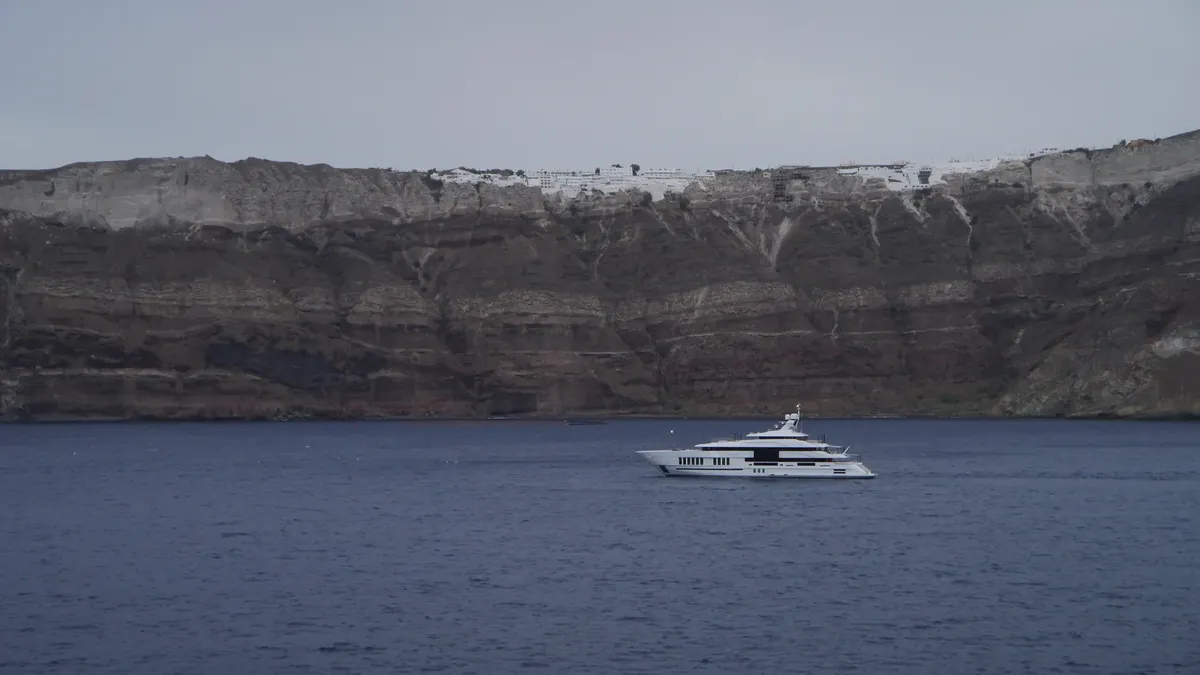 A luxury yacht cruises by the stunning cliffs of Santorini, Greece under a clear sky.