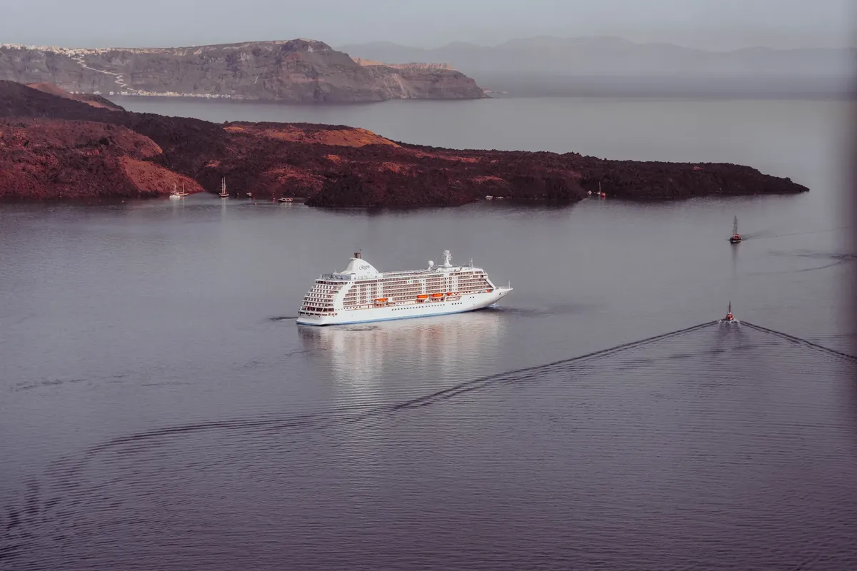 Aerial view of a majestic cruise ship sailing near the volcanic coast of Santorini's caldera.